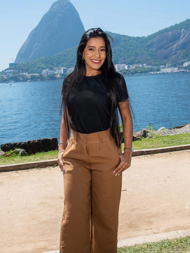 Daniella Hollanda, psicóloga, sorrindo, em frente à Baía de Guanabara
